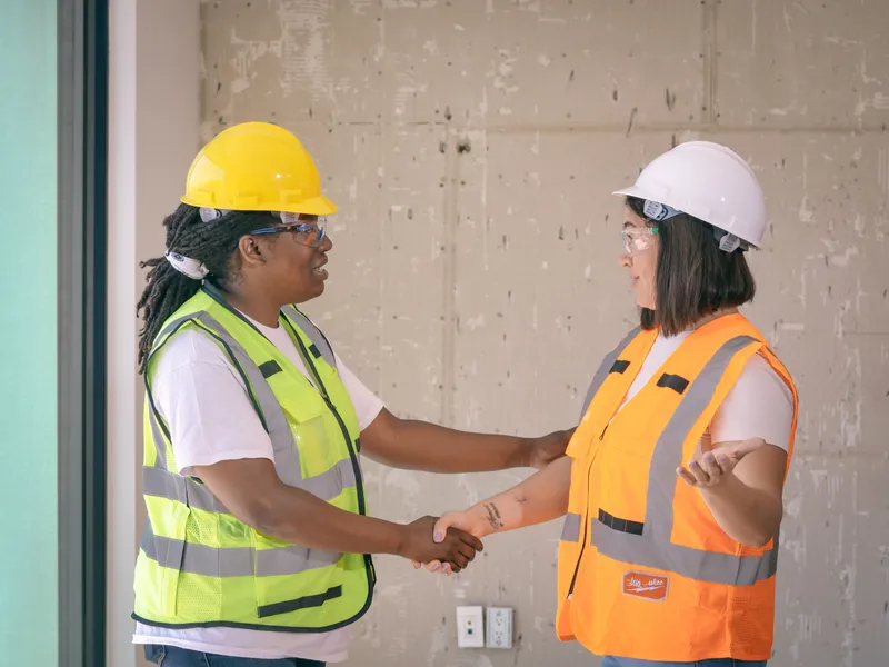 Two workers in safety gear shaking hands on a finished job